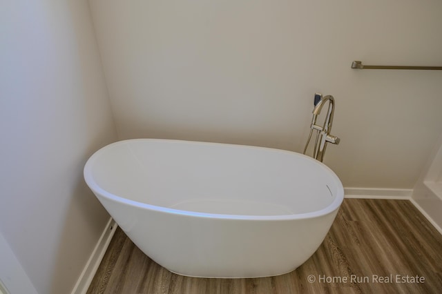 bathroom with wood finished floors, a freestanding tub, and baseboards