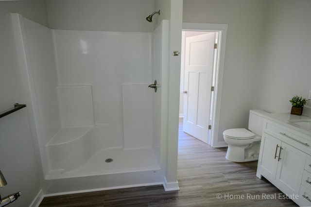full bathroom featuring a shower, wood finished floors, toilet, vanity, and baseboards