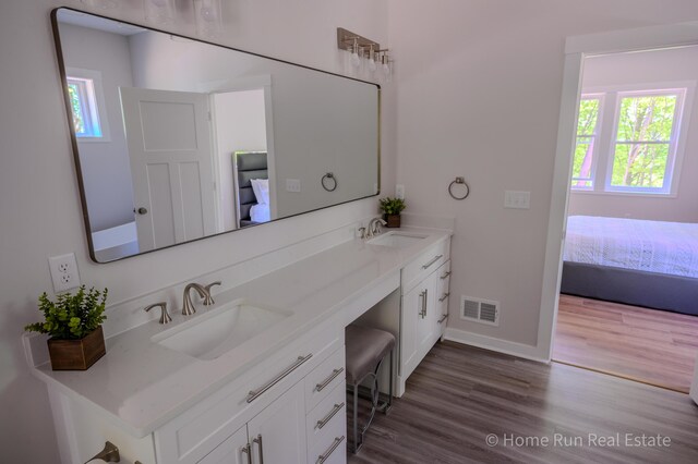 ensuite bathroom featuring double vanity, wood finished floors, and baseboards