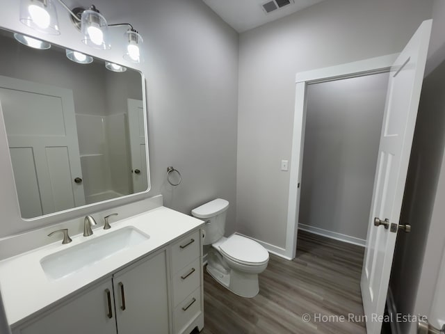 bathroom featuring toilet, wood finished floors, vanity, baseboards, and a shower