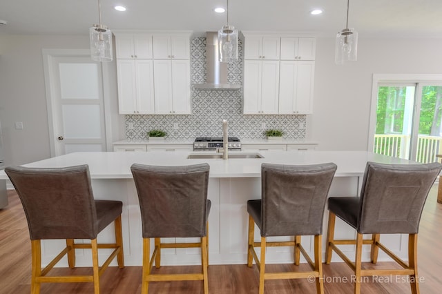 8828 Division Ave S, Byron Center, MI 49315 - kitchen featuring wall chimney exhaust hood, a sink, decorative backsplash, a center island with sink, and light countertops