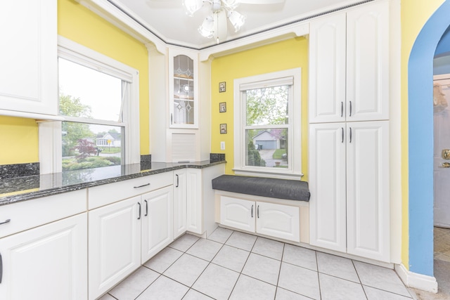 885 Hawthorne Ave, Ypsilanti, MI 48198 - kitchen featuring arched walkways, dark stone countertops, light tile patterned floors, glass insert cabinets, and white cabinetry