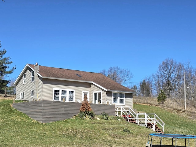 back of property with a chimney, a lawn, and a trampoline