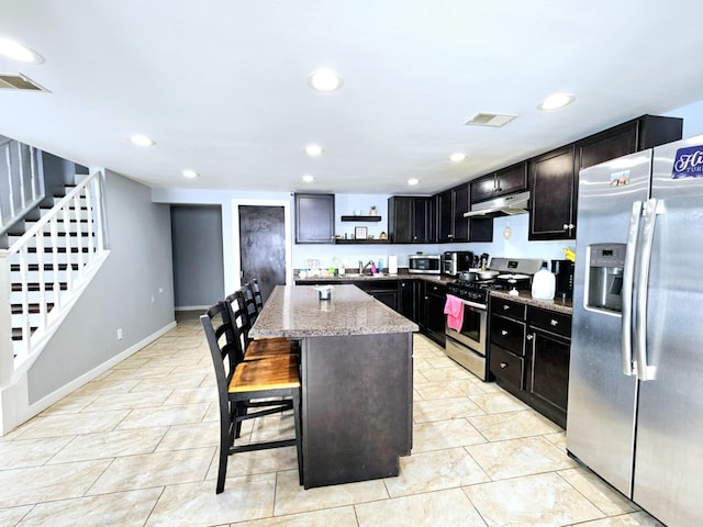 kitchen featuring appliances with stainless steel finishes, under cabinet range hood, light stone countertops, a center island, and recessed lighting