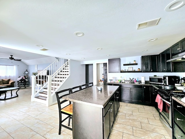 kitchen with appliances with stainless steel finishes, a kitchen breakfast bar, a center island, under cabinet range hood, and open shelves