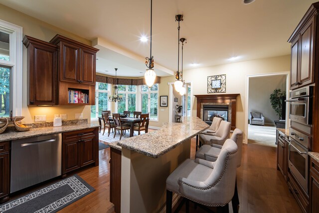 8307 Granite Ct, Dexter, MI 48130 - kitchen featuring stainless steel appliances, a breakfast bar, dark wood-style floors, a tile fireplace, and light stone counters