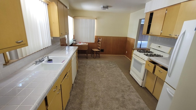 kitchen with white appliances, tile countertops, a wainscoted wall, a sink, and wood walls