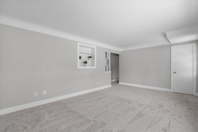 spare room featuring built in shelves, carpet flooring, and baseboards