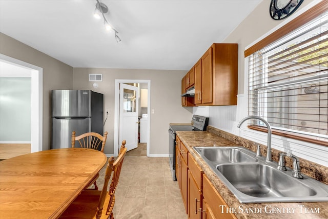 kitchen with stainless steel appliances, a sink, under cabinet range hood, brown cabinets, and washer / dryer
