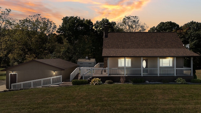 back of property featuring a lawn, a chimney, an outbuilding, covered porch, and a shingled roof