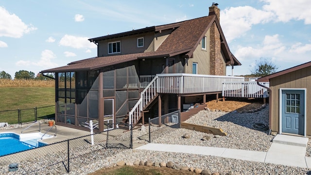 rear view of house with a wooden deck, roof with shingles, a sunroom, a chimney, and a patio