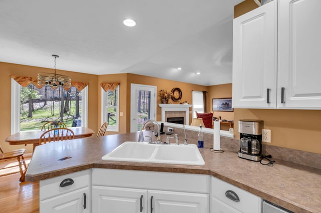 9100 Boggie Dr Unit 159, Canadian Lakes, MI 49346 - kitchen with a sink, a peninsula, a chandelier, a tiled fireplace, and white cabinets