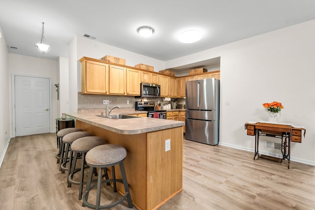 kitchen with appliances with stainless steel finishes, a peninsula, a sink, a breakfast bar area, and light wood-style floors