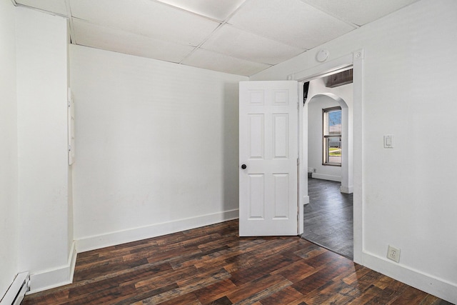 601 N Rath Ave, Ludington, MI 49431 - unfurnished room featuring a baseboard radiator, arched walkways, baseboards, dark wood-type flooring, and a paneled ceiling