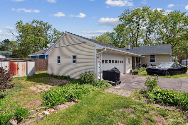 view of home's exterior with an attached garage, driveway, a storage shed, fence, and an outdoor structure