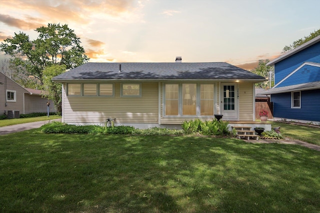 back of property with a yard, central AC, and roof with shingles