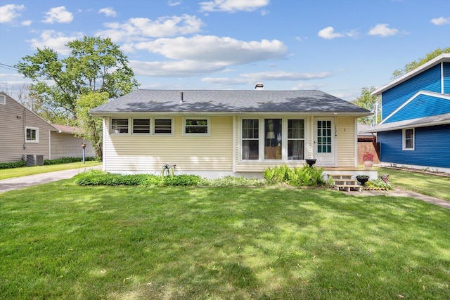 rear view of property with a lawn, roof with shingles, and central AC unit