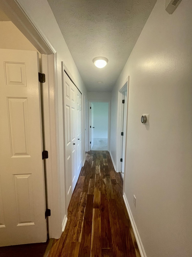 corridor with dark wood-style floors, a textured ceiling, and baseboards
