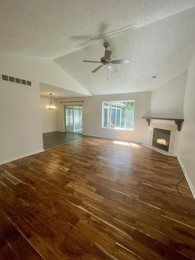 unfurnished living room featuring a tile fireplace, wood finished floors, vaulted ceiling, a ceiling fan, and a textured ceiling