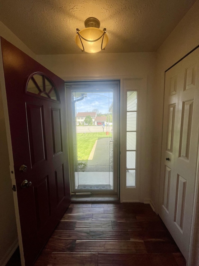 doorway to outside with dark wood-style floors and a textured ceiling