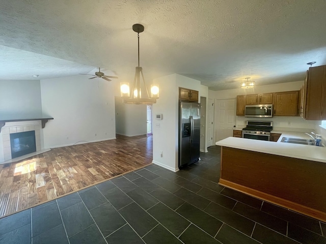kitchen with stainless steel appliances, a sink, open floor plan, brown cabinets, and a textured ceiling