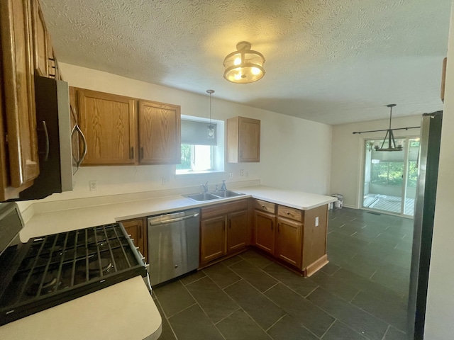 kitchen with appliances with stainless steel finishes, a peninsula, a sink, decorative light fixtures, and a textured ceiling