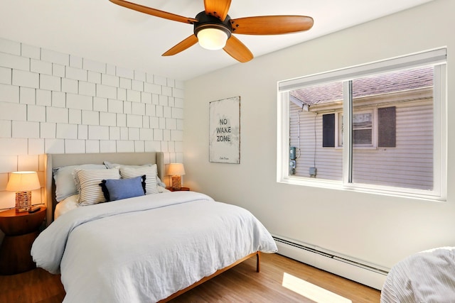 bedroom featuring a baseboard heating unit, wood finished floors, and ceiling fan