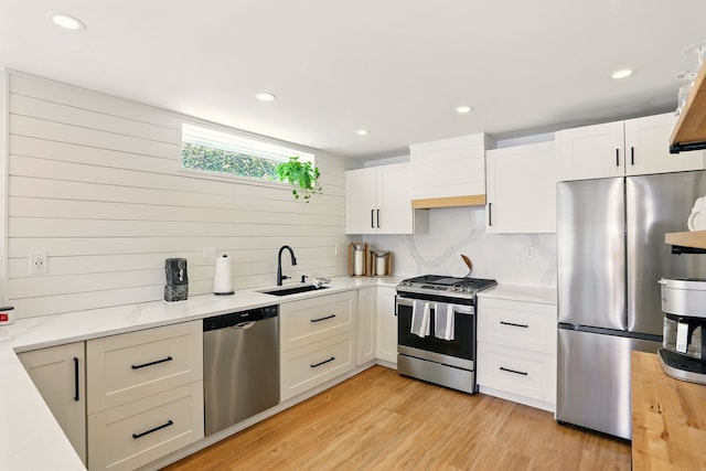 kitchen with appliances with stainless steel finishes, a sink, white cabinetry, light wood-type flooring, and recessed lighting