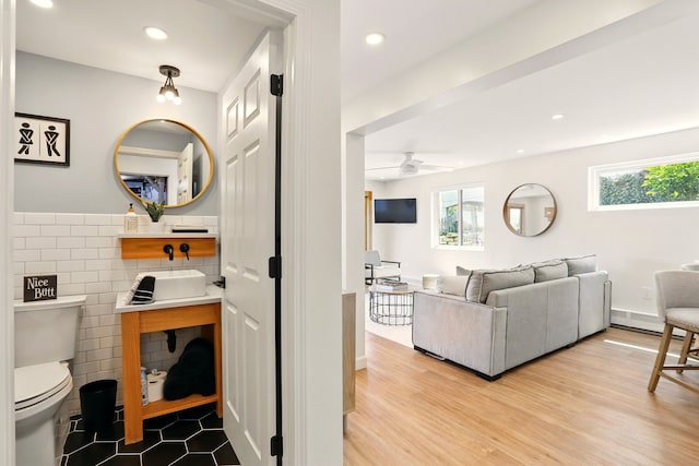 living area featuring tile walls, healthy amount of natural light, wainscoting, ceiling fan, and wood finished floors