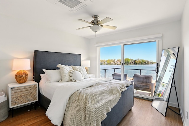 bedroom with access to exterior, a water view, wood finished floors, and a ceiling fan