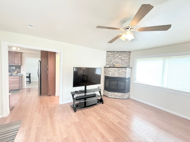 living area with baseboards, light wood-style floors, a ceiling fan, and a fireplace