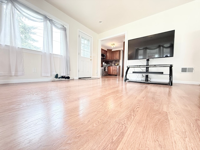 unfurnished living room with light wood-type flooring, plenty of natural light, and baseboards