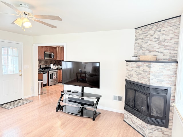 living area with light wood finished floors, ceiling fan, baseboards, and a large fireplace