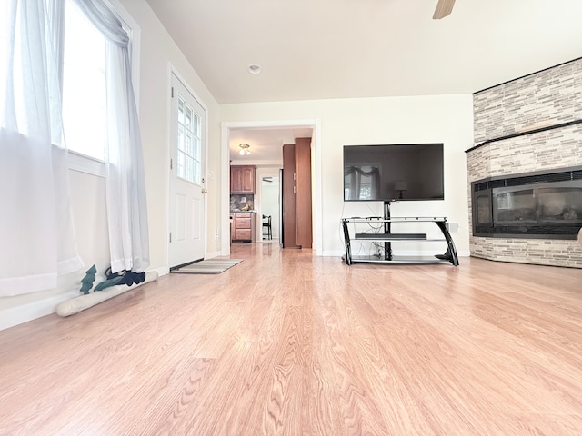 unfurnished living room featuring light wood-style floors, ceiling fan, baseboards, and a glass covered fireplace