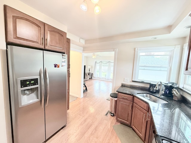 kitchen with stainless steel fridge, a sink, light wood-style floors, dark stone countertops, and brown cabinets