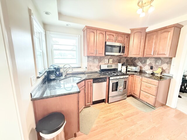 kitchen featuring appliances with stainless steel finishes, a sink, dark stone countertops, decorative backsplash, and light wood finished floors