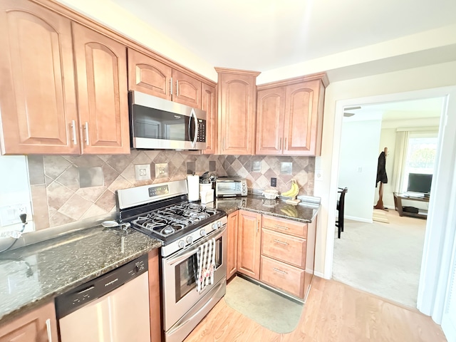 kitchen with stainless steel appliances, dark stone counters, light brown cabinetry, and decorative backsplash