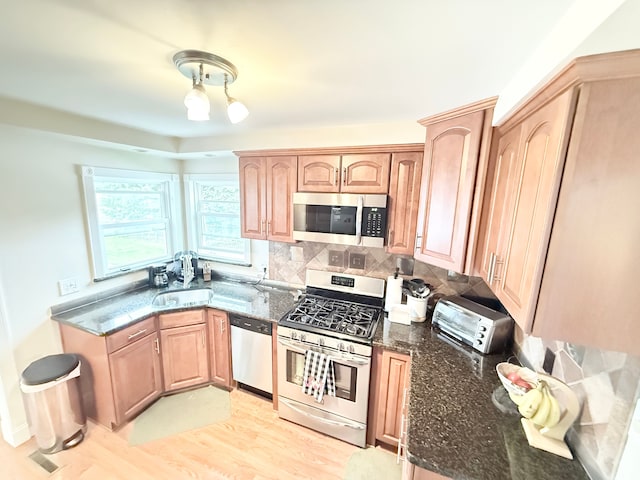 kitchen featuring stainless steel appliances, a sink, dark stone counters, light wood-type flooring, and light brown cabinets