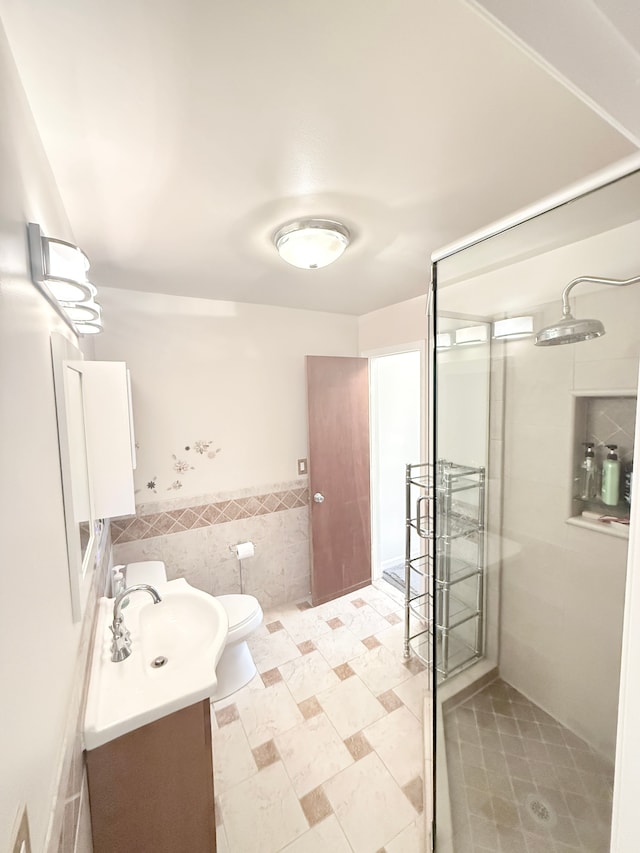 full bathroom with tile walls, vanity, a shower stall, toilet, and wainscoting