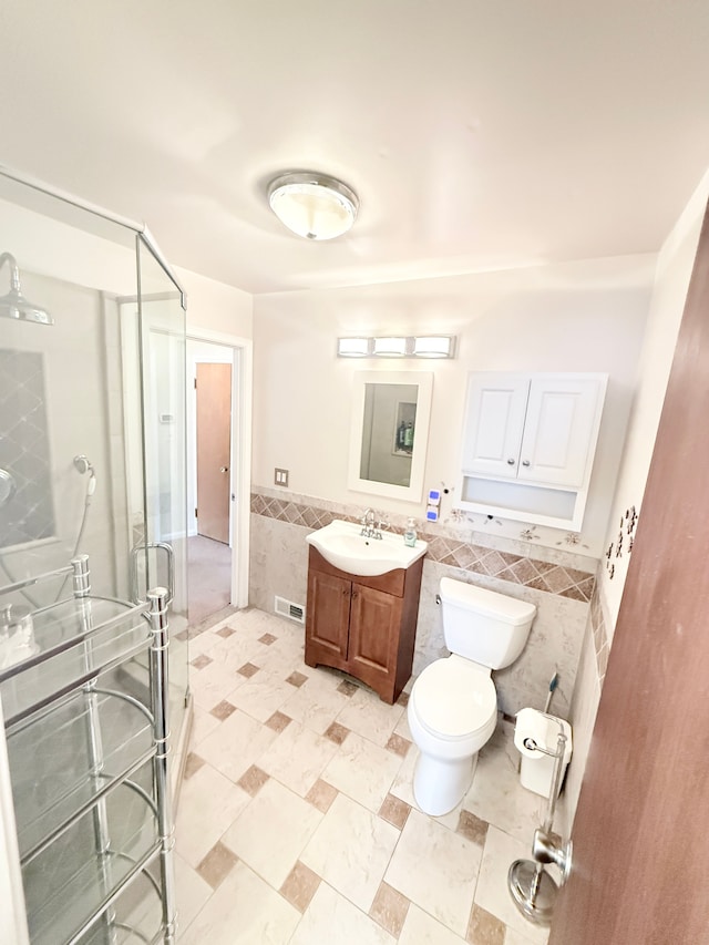 full bath featuring tile walls, a stall shower, vanity, toilet, and a wainscoted wall