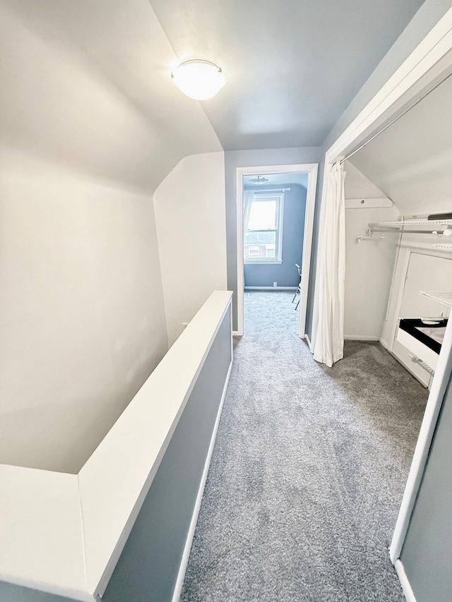 hall with carpet floors, vaulted ceiling, and an upstairs landing