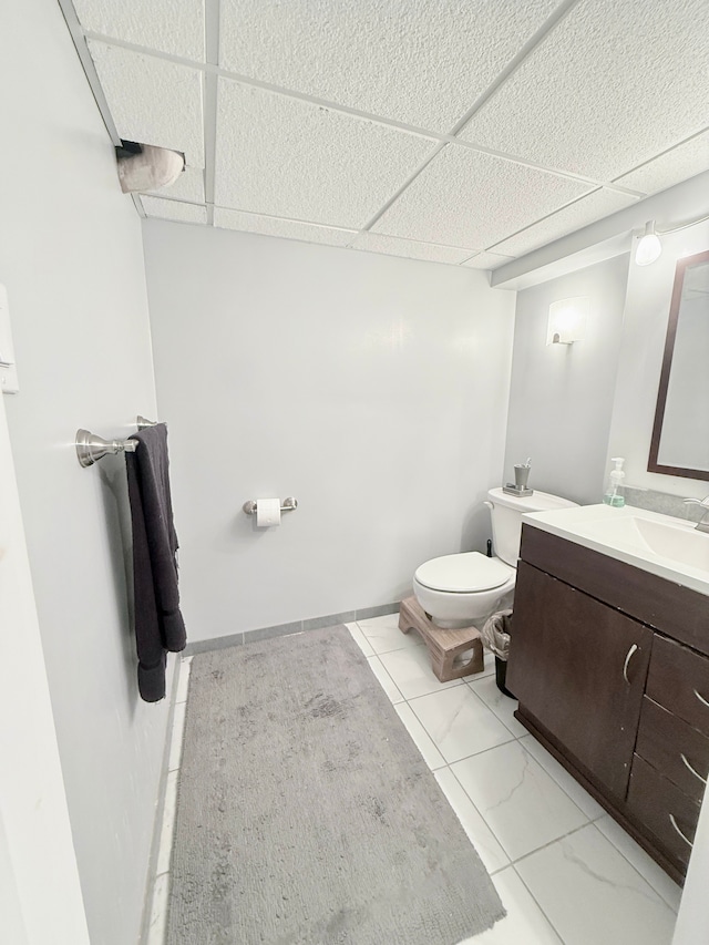 half bath featuring a paneled ceiling, toilet, and vanity