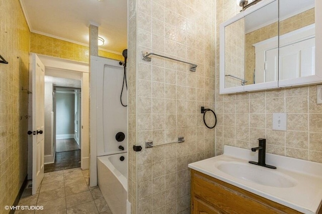 bathroom with tile walls, crown molding, vanity, and tub / shower combination