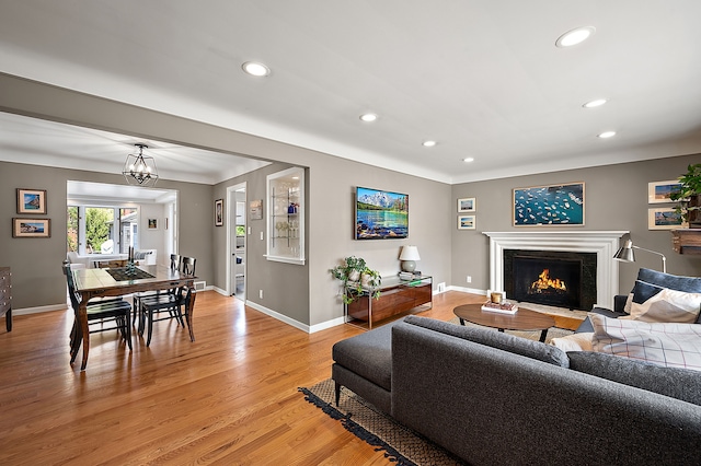 living room with recessed lighting, a fireplace with flush hearth, baseboards, and light wood-style flooring