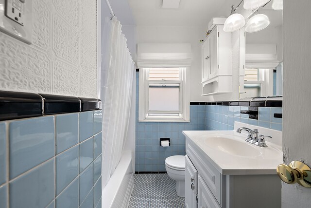 full bathroom with plenty of natural light, tile walls, toilet, vanity, and wainscoting