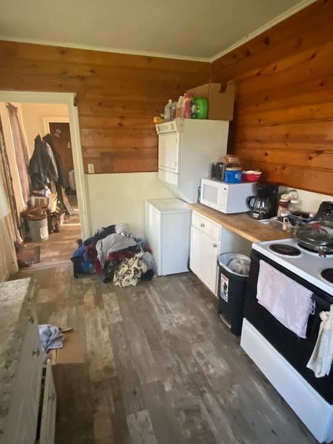 437 W Mount Morris St, Mount Morris, MI 48458 - kitchen with electric stove, wooden walls, white microwave, dark wood-style flooring, and estacked washer and dryer