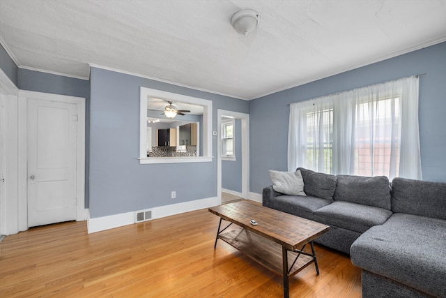 living area with ornamental molding, plenty of natural light, light wood-type flooring, baseboards, and ceiling fan