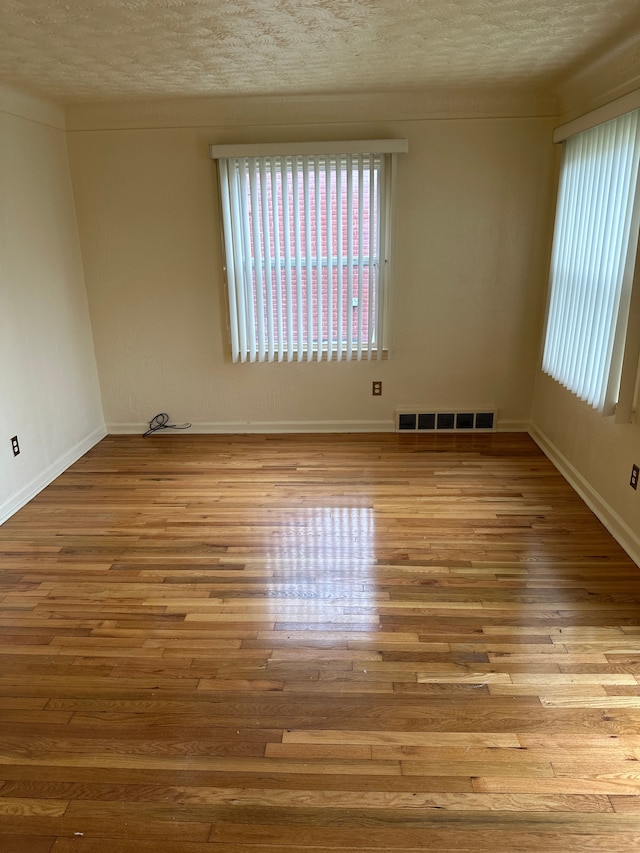 unfurnished room with healthy amount of natural light, wood finished floors, a textured ceiling, and baseboards
