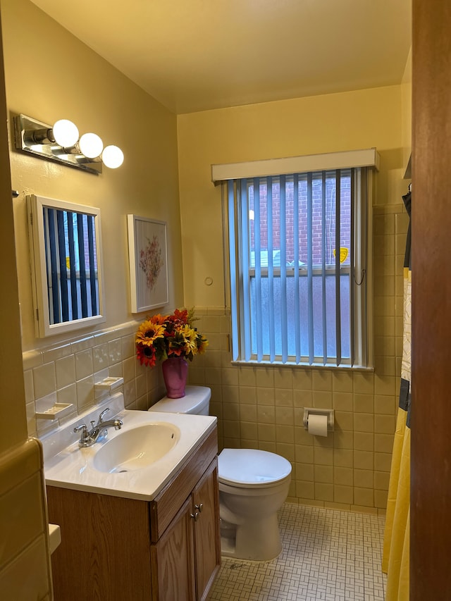 bathroom with tile walls, toilet, vanity, tile patterned flooring, and wainscoting