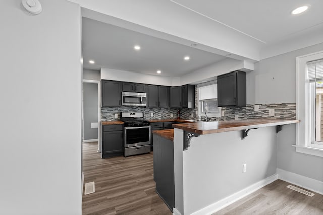 kitchen with appliances with stainless steel finishes, a breakfast bar area, backsplash, dark wood-type flooring, and recessed lighting